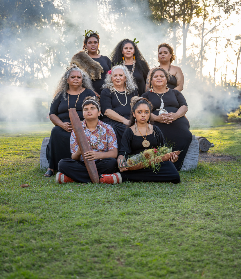 A group of First Nations women and children gathered outdoors in soft morning smoke